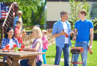 Portrait of young men frying sausages and talking in the countryside at weekend with their families near by